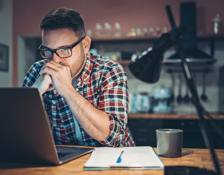 person sitting at a desk focusing on their laptop with a pen and notepad